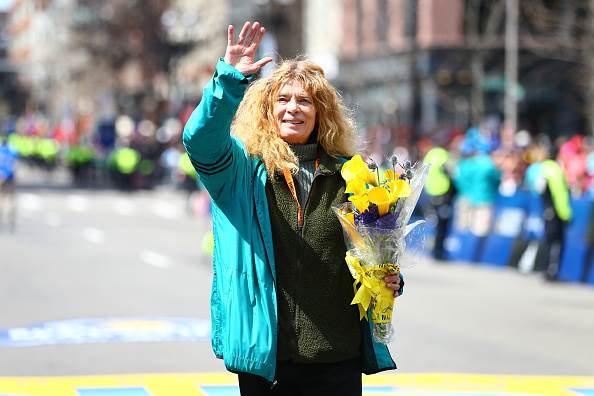 Bobbi Gibb, waving to crowd and holding flowers at the finish line at Boston Marathon on April 18, 2016